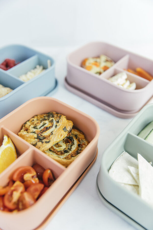 four coloured baby lunchboxes wach with food in